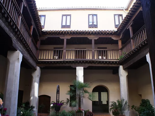 Patio interior con dos alturas de galerías de madera y plantas ornamentales.