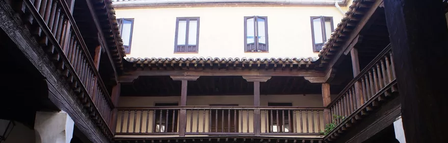 Patio interior con dos alturas de galerías de madera y plantas ornamentales.