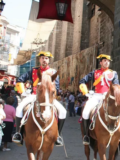 Jinetes con uniforme desfilando junto a grandes tapices