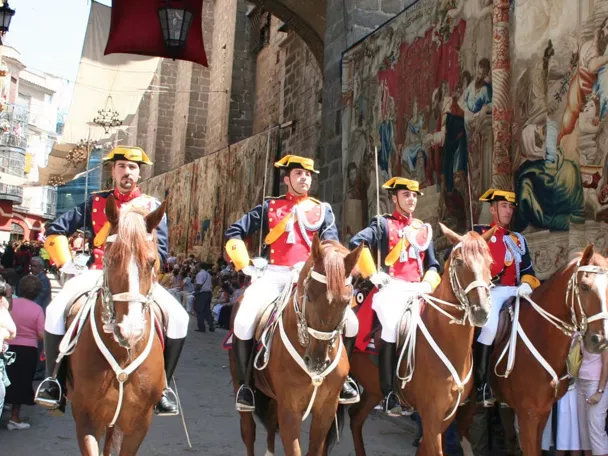 Jinetes con uniforme desfilando junto a grandes tapices