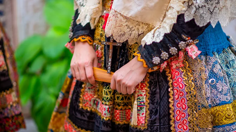 Detalle de traje tradicional bordado con joyería y abanico en las manos