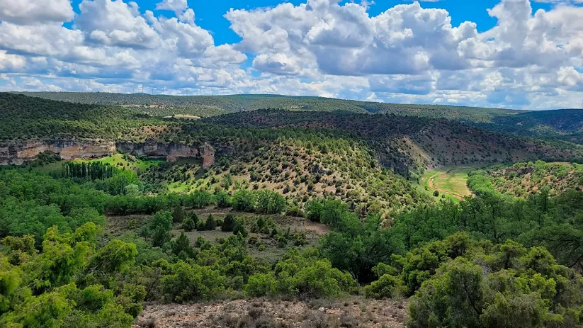 Paisaje de valle con laderas verdes y cielo nuboso