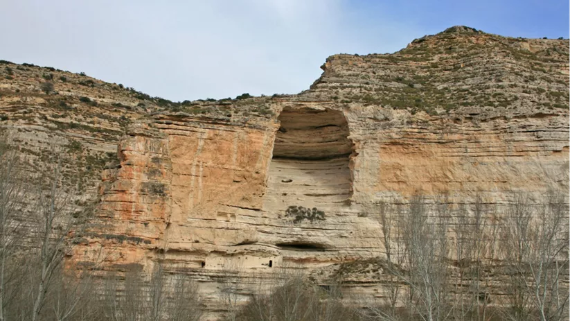 Acantilado erosionado con gran cavidad central y árboles en primer plano.