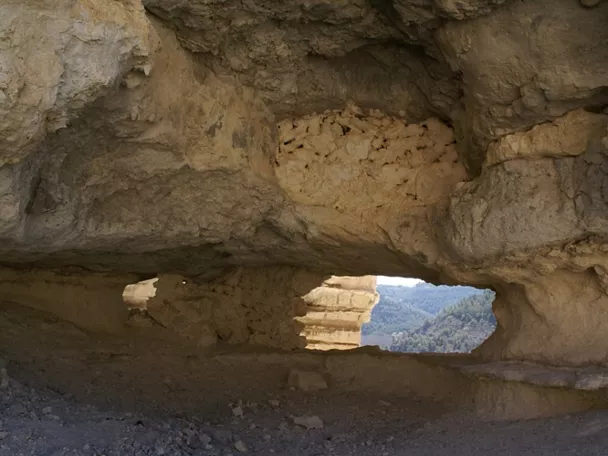 Interior de cueva excavada en roca con abertura hacia un valle boscoso.