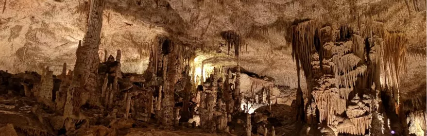 Gran sala subterránea con abundantes estalactitas y estalagmitas iluminadas.
