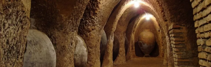 Galería subterránea con tinajas de barro bajo arcos.