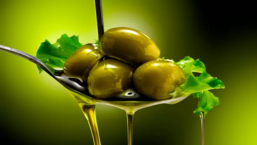 Aceitunas verdes sobre cuchara con aceite de oliva goteando