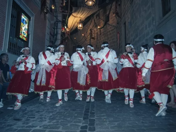 Danzantes con trajes rojos bailando en una calle iluminada de noche.