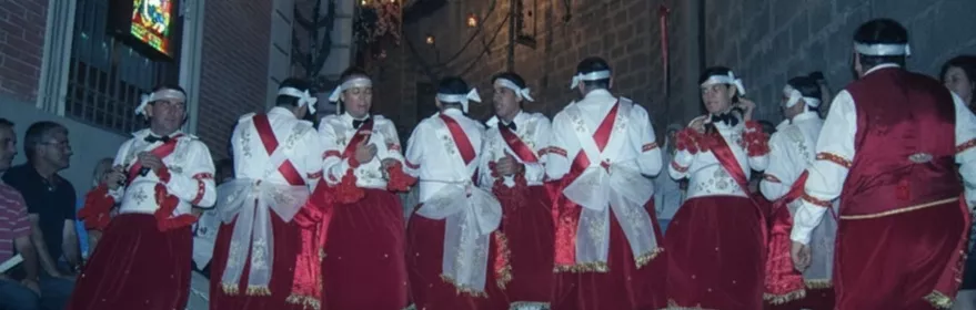 Danzantes con trajes rojos bailando en una calle iluminada de noche.