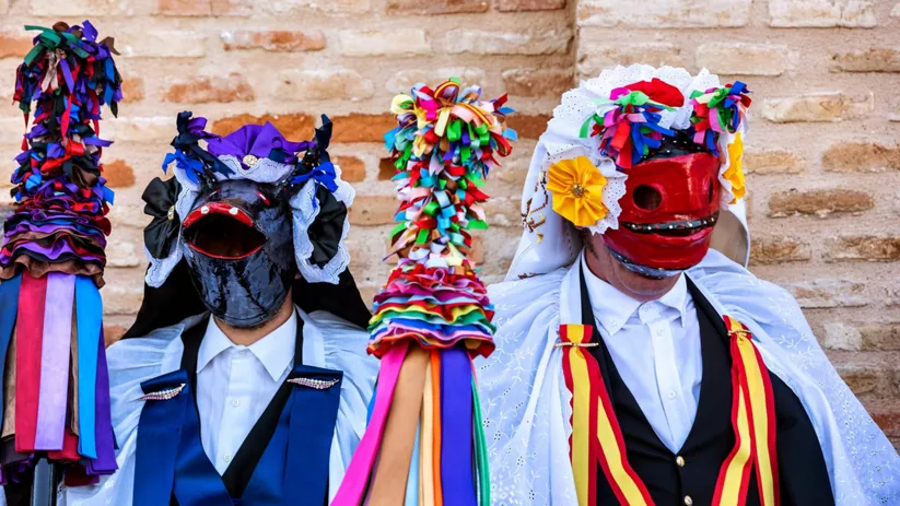 Personas con máscaras coloridas y bastones decorados posando ante un muro.
