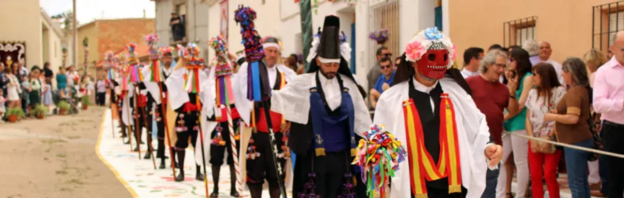 Desfile tradicional con personas enmascaradas caminando sobre alfombra decorada.