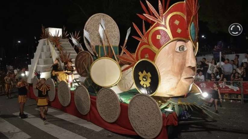 Carroza colorida con gran rostro y escudos decorativos desfilando entre público.