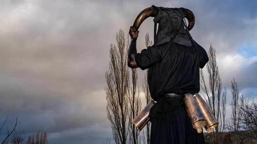 Figura con cuernos y cencerros bajo cielo nublado.