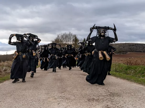 Personas disfrazadas de negro con cuernos corriendo por camino rural.