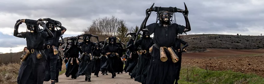 Personas disfrazadas de negro con cuernos corriendo por camino rural.