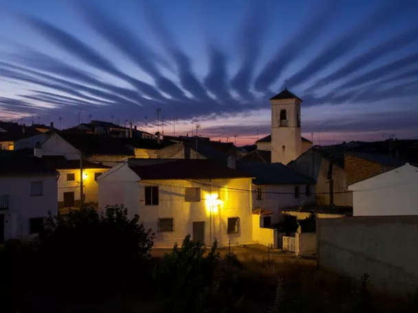 Vista nocturna del pueblo, con casas encaladas iluminadas y una torre sobresaliendo bajo un cielo azul intenso.