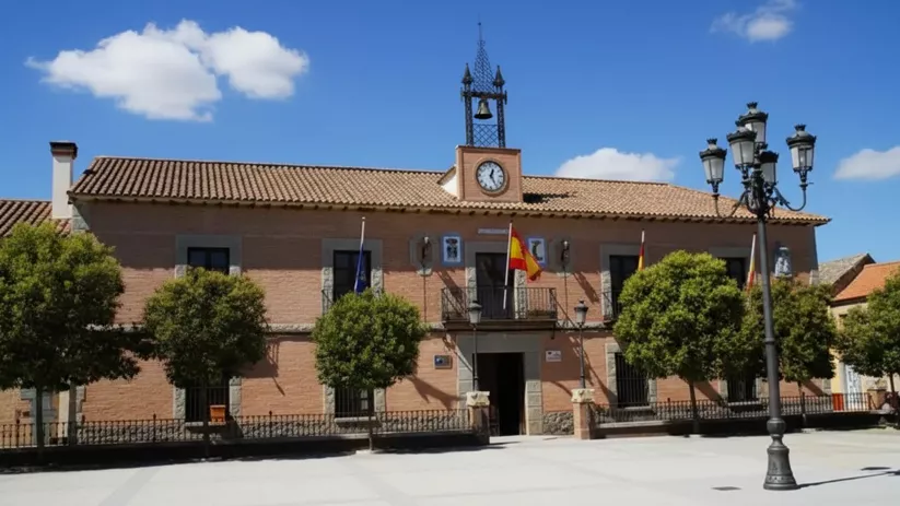 Edificio institucional en plaza abierta, con fachada simétrica, reloj central y arbolado alineado.