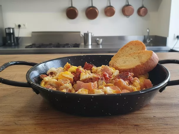 Revuelto de huevo con carne y embutido servido en sartén tradicional