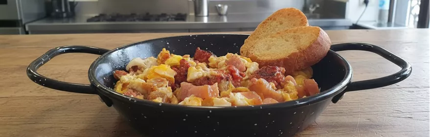 Revuelto de huevo con carne y embutido servido en sartén tradicional