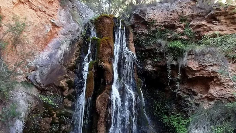 Salto de agua rodeado de rocas y vegetación frondosa.