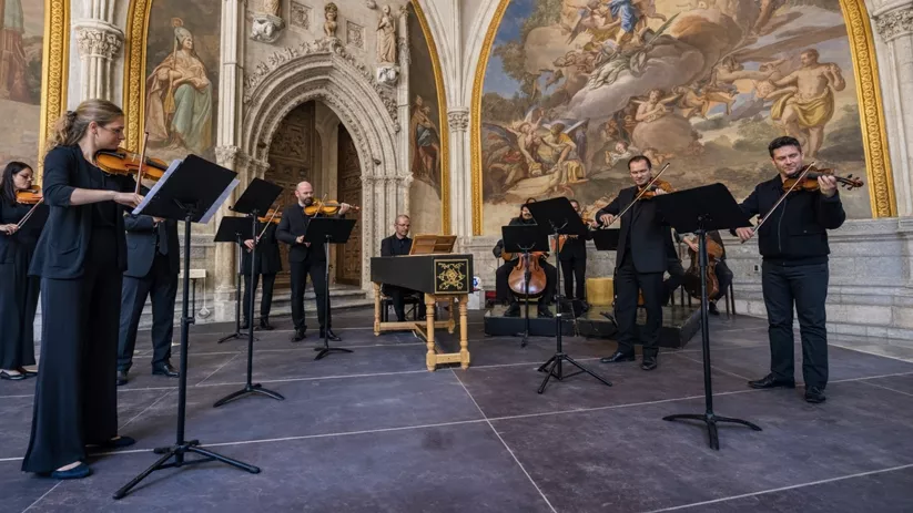 Conjunto de músicos de cuerda actuando bajo arcos con frescos en un edificio histórico.