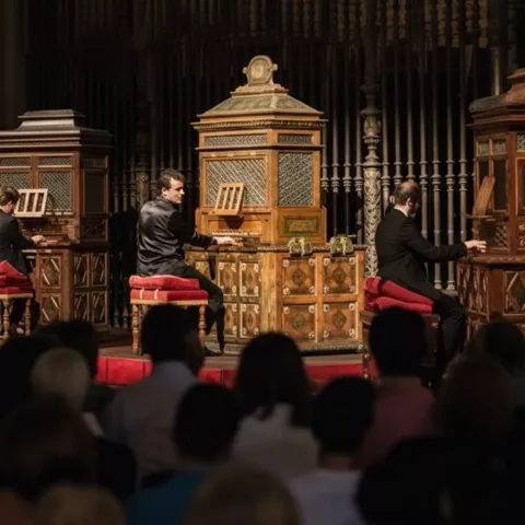 Tres músicos tocando órganos históricos ante un público en penumbra.