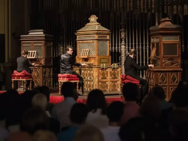Tres músicos tocando órganos históricos ante un público en penumbra.