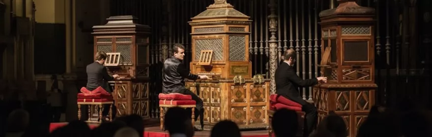 Tres músicos tocando órganos históricos ante un público en penumbra.