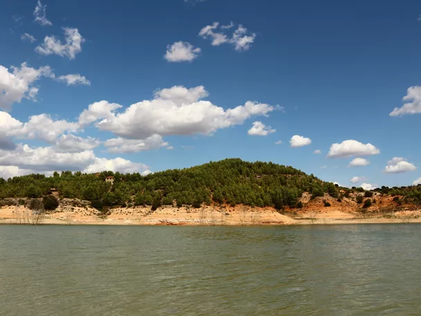 Embalse rodeado de colinas verdes bajo cielo azul con nubes.