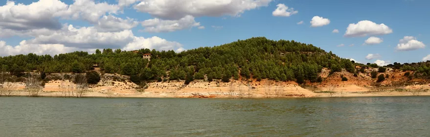 Embalse rodeado de colinas verdes bajo cielo azul con nubes.