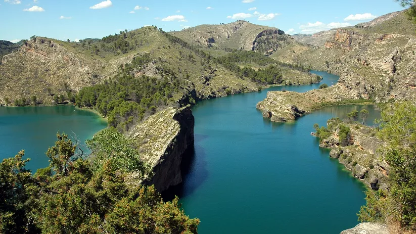 Embalse de aguas turquesas entre cañones rocosos y vegetación mediterránea.