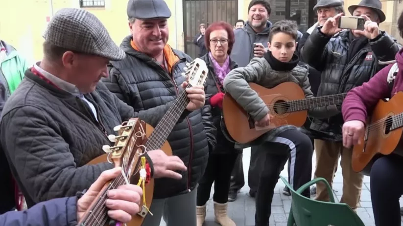 Hombre y joven tocando guitarras rodeados de público.