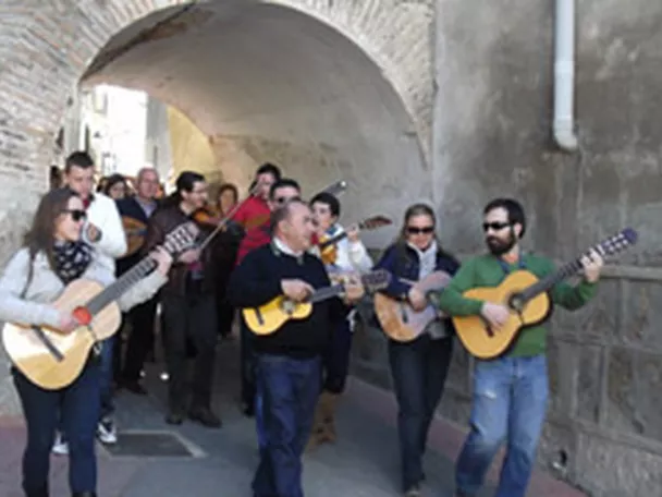 Pasacalles de músicos con guitarras bajo un arco de piedra.