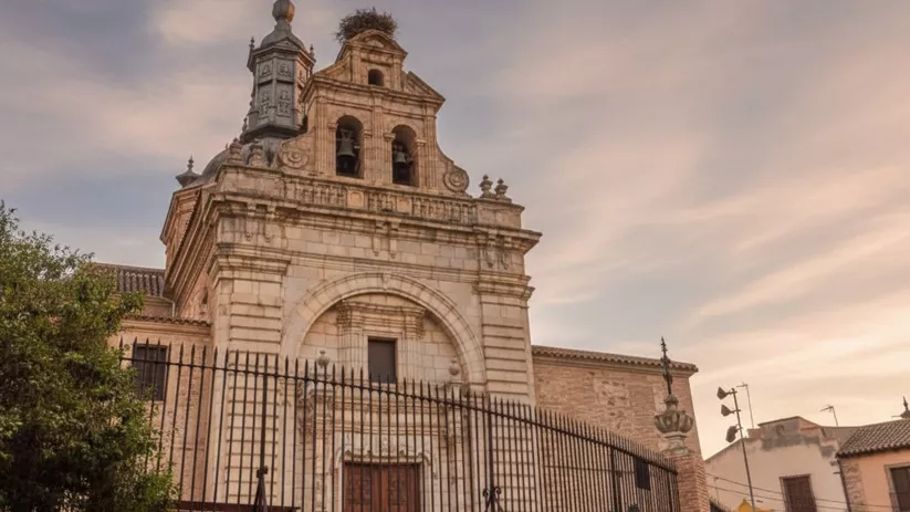 Entrada principal de templo con arco decorado y verja de hierro en plaza urbana.