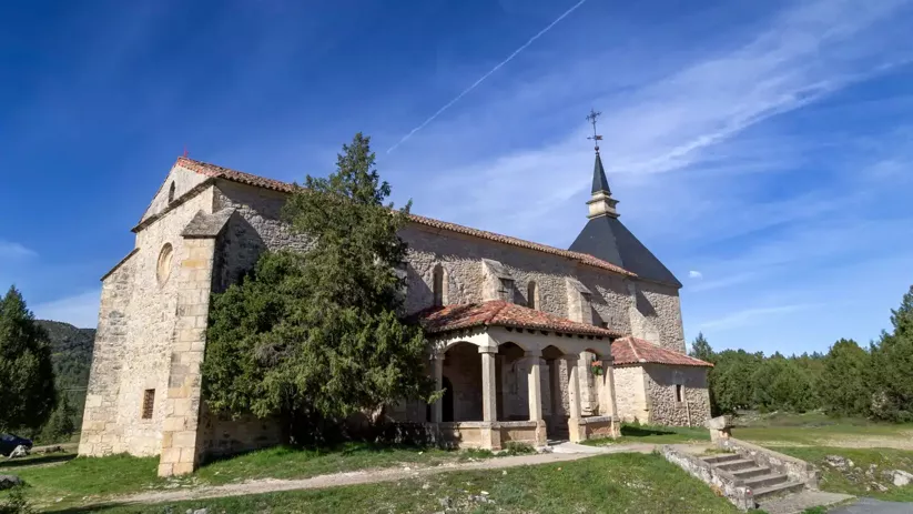 Iglesia rural de piedra con pórtico y torre bajo cielo azul.