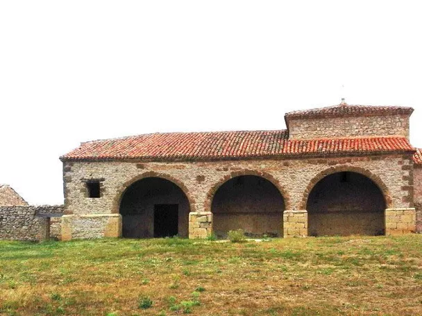 Ermita rural de piedra con pórtico de arcos en paisaje abierto