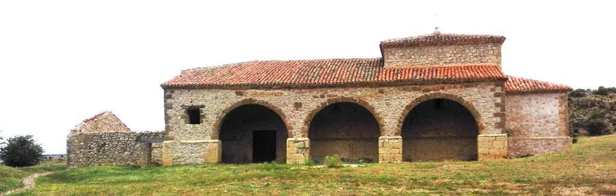 Ermita rural de piedra con pórtico de arcos en paisaje abierto