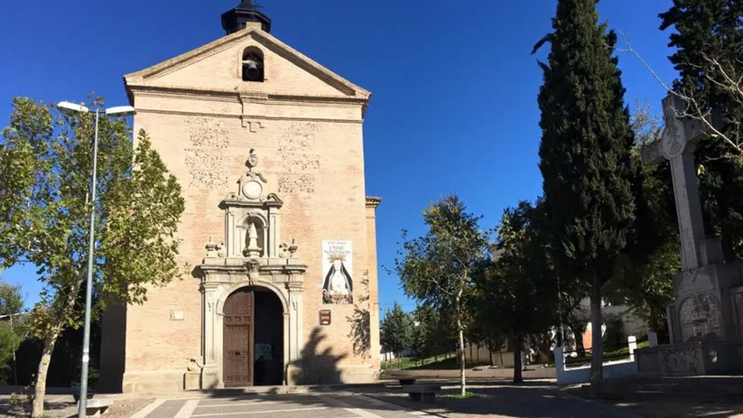 Fachada de iglesia de ladrillo con portada de piedra y plaza delante.
