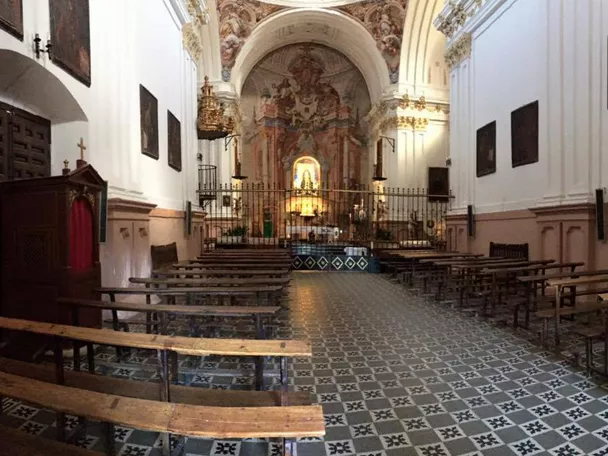 Interior de iglesia con bancos de madera y pavimento decorado.