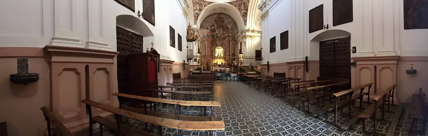 Interior de iglesia con bancos de madera y pavimento decorado.