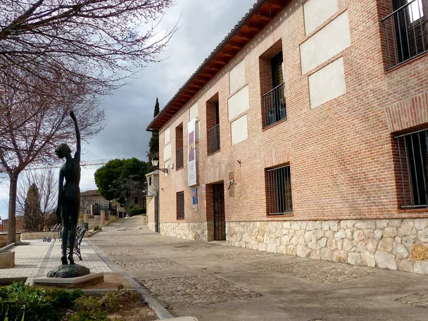 Fachada de ladrillo con balcones y escultura en la plaza.