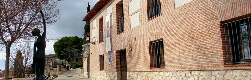 Fachada de ladrillo con balcones y escultura en la plaza.