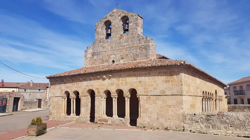 Iglesia de piedra con pórtico de arcos y torre campanario.