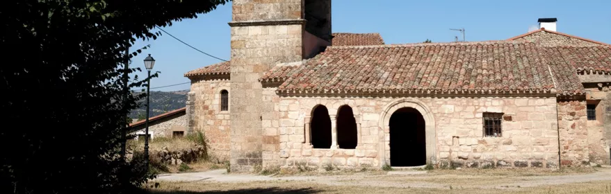 Iglesia de piedra con espadaña y pórtico de arcos.