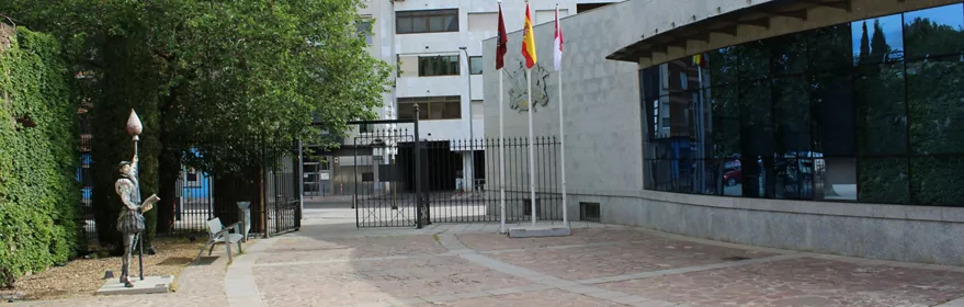 Plaza urbana con edificio cultural moderno, zona ajardinada y banderas