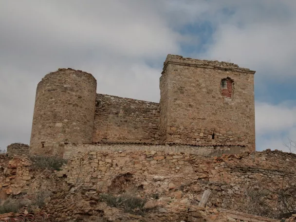 Muralla de piedra con torre circular en ruinas.