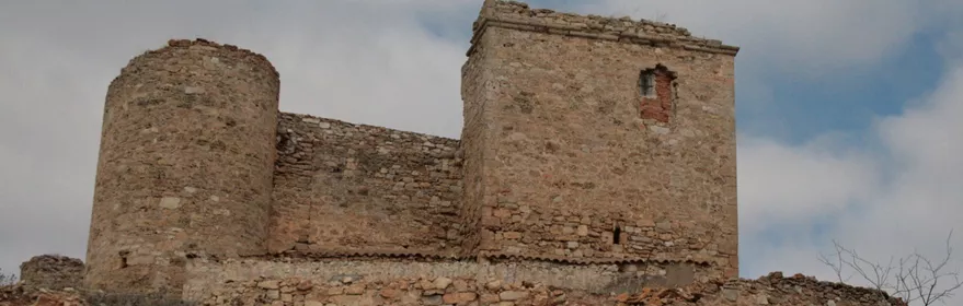 Muralla de piedra con torre circular en ruinas.
