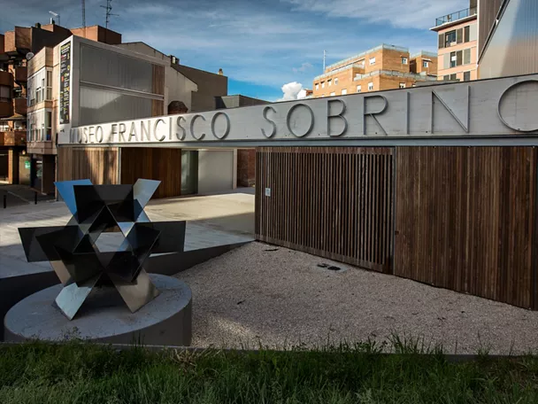 Fachada moderna con rótulo metálico y escultura geométrica.