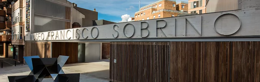 Fachada moderna con rótulo metálico y escultura geométrica.