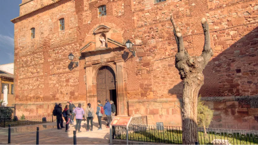 Fachada de iglesia de piedra con torre y visitantes